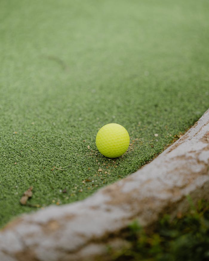 services-03 Close-up of a yellow golf ball on green artificial turf, ready for play.