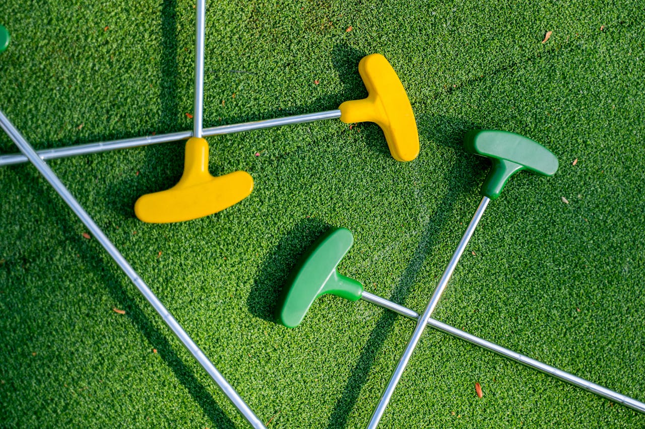 services-04 Vibrant yellow and green mini golf putters arranged on a lush green turf, perfect for leisure scenes.
