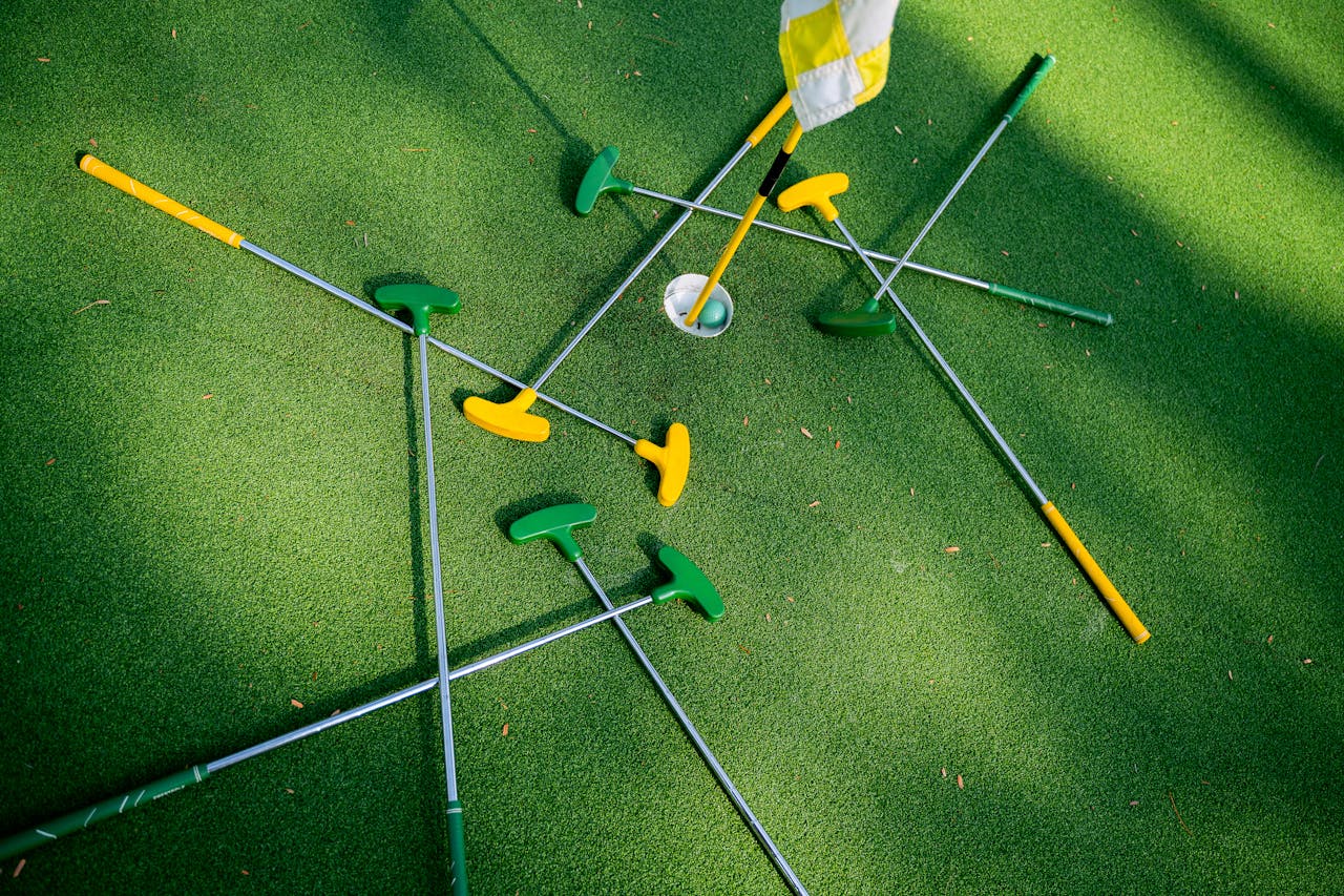Top view of colorful putters scattered around a golf hole on lush green grass.