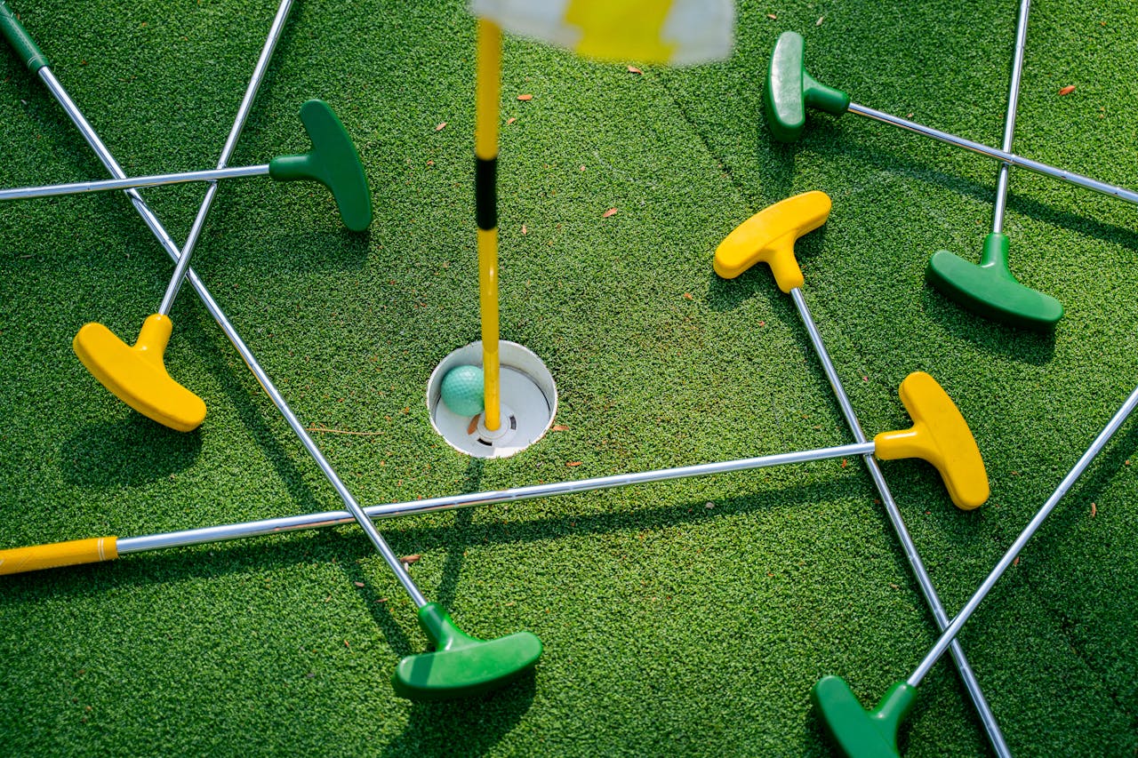 hero-img Top view of colorful mini golf putters around a hole on artificial grass.