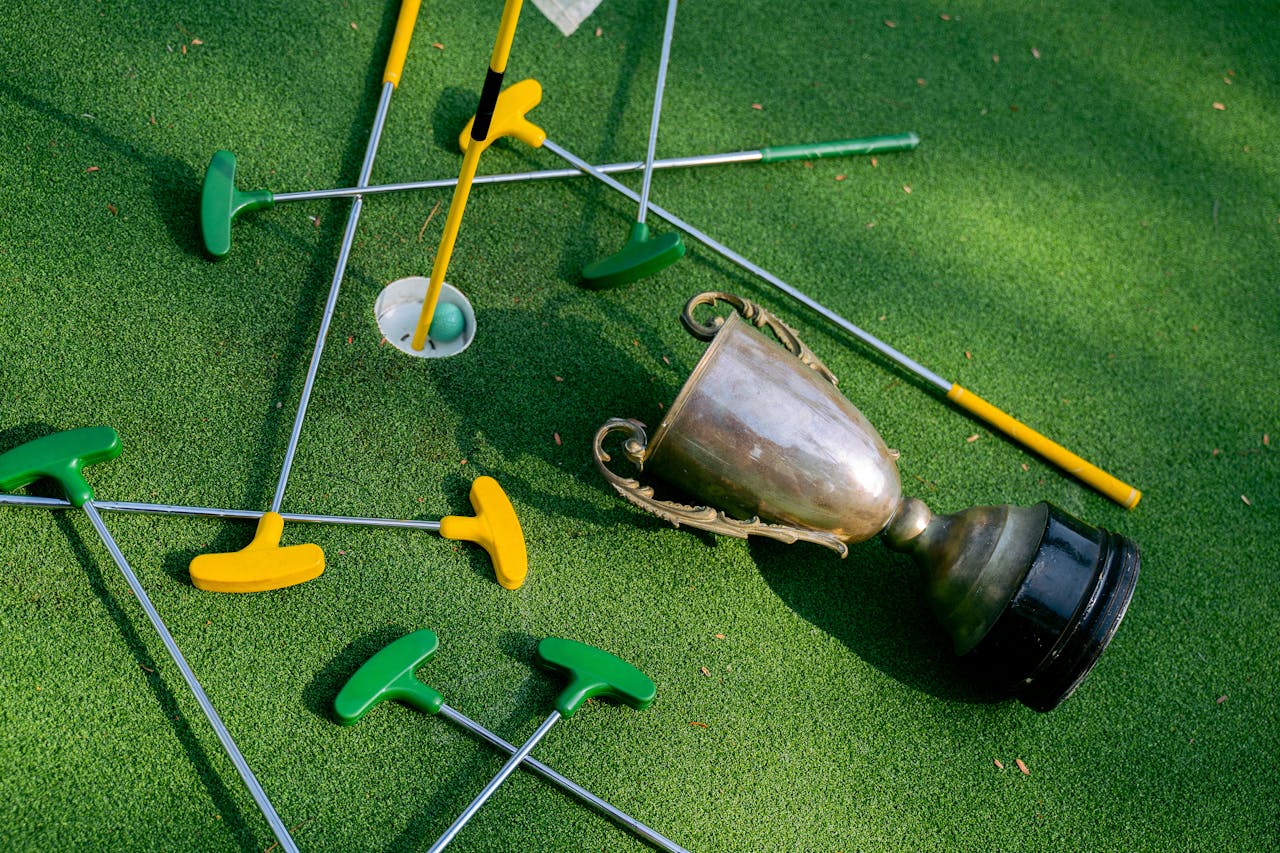 about-01 Colorful mini golf putters with a trophy on vibrant green turf, symbolizing victory.