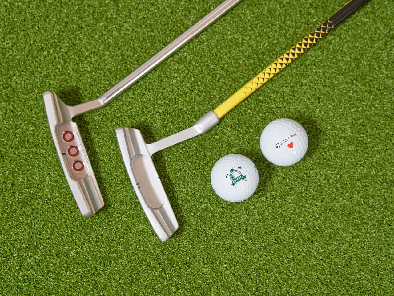 services-01 Two golf putters and golf balls placed on artificial turf, ideal for practice.